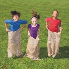 three children are standing in the grass with their hands on their hipss and one is holding a sack