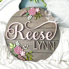 a wooden sign that says reese lynn with pink flowers on the front and green leaves around it