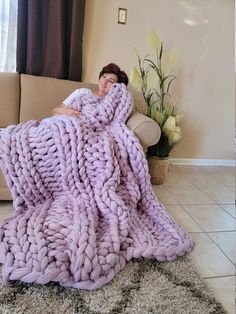 a woman is wrapped in a giant chunky blanket while sitting on a couch with her eyes closed