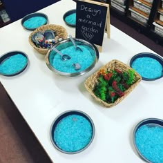 bowls filled with blue colored sand on top of a white table next to baskets full of seaweed