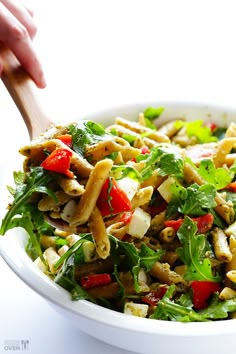 a salad in a white bowl with a wooden spoon on the side and someone's hand reaching for it