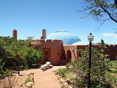 an adobe - style house in the desert surrounded by trees and bushes with a blue dome on top