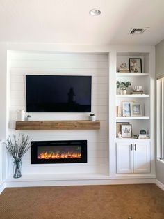 a living room with white walls and a fireplace in the center, built - in shelving