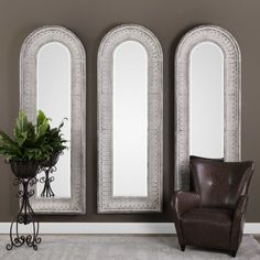 two mirrors and a chair in front of a wall with three arched windows on it