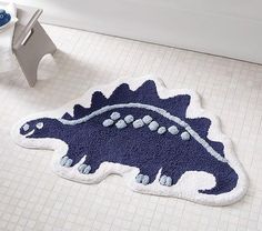 a bathroom rug with a blue dinosaur design on the floor next to a bathtub