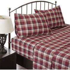 a bed with red and white plaid sheets in a bedroom next to a lamp on a night stand