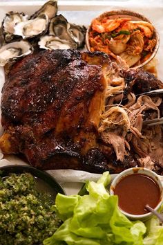 a large piece of meat on a plate next to some vegetables and dipping sauces