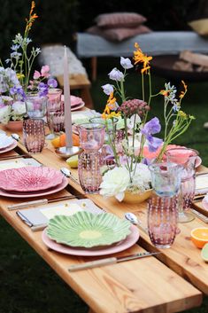 an outdoor table set with plates, flowers and candles for a party or gathering in the garden