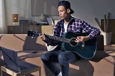 a man sitting on top of a couch holding a guitar next to a laptop computer