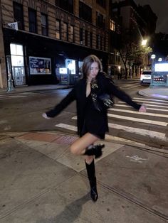 a woman is dancing on the sidewalk in front of a crosswalk at night time