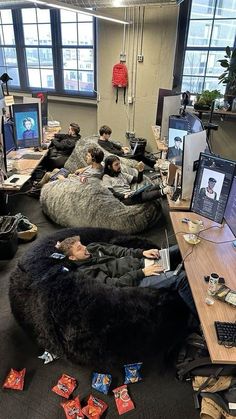 people sleeping on bean bag chairs in an office space with computers and other items scattered about