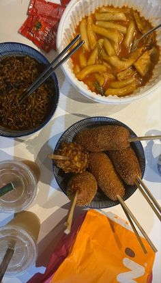 three bowls filled with food and chopsticks on top of a white tablecloth