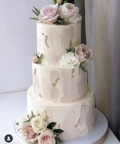 a three tiered wedding cake with flowers on the top and bottom, sitting on a table