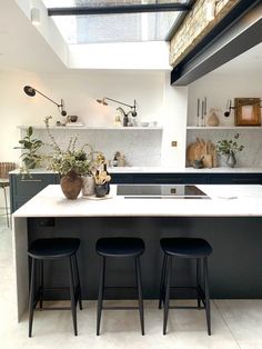 an open kitchen with three stools in front of the counter and two plants on the island