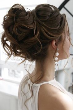 a woman with her hair in a low bun and pearls on the earrings is looking out the window