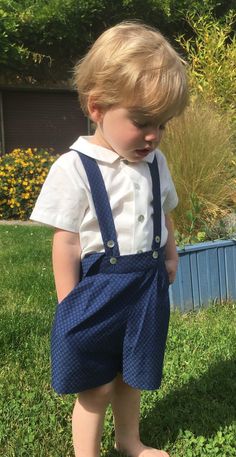 a young boy in blue shorts and white shirt standing on grass with his feet up