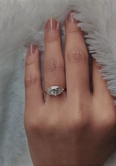 a woman's hand with a diamond ring on top of her finger, in front of white fur