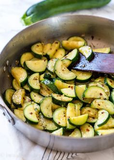 a pan filled with zucchini and sliced cucumbers next to a wooden spoon