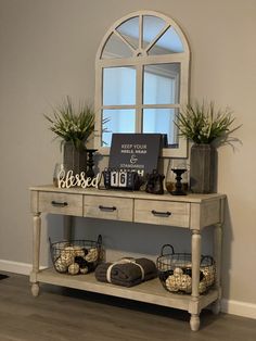 a white table with baskets and plants on it in front of a large arched window