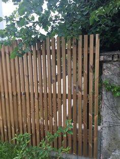 a wooden fence in front of a stone wall and green plants on the other side