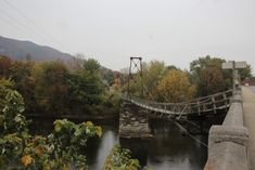 a bridge over a river in the middle of autumn with trees and hills behind it