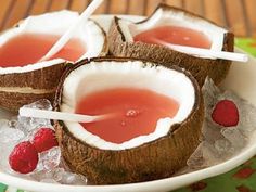 three coconuts with raspberries are on a plate and one is filled with watermelon