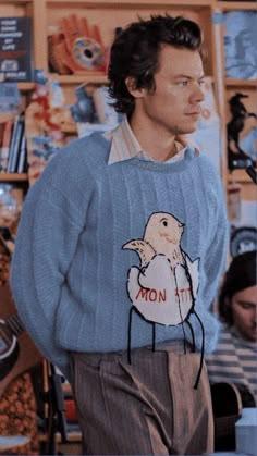 a man in a blue sweater with a bird on it standing next to a store shelf