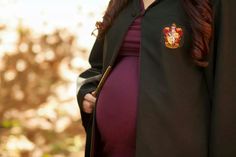 a pregnant woman wearing a harry potter robe and holding her hand on her hip while standing in front of trees