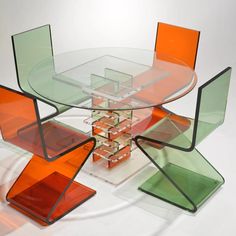 a glass table with orange and green chairs around it on top of a white surface