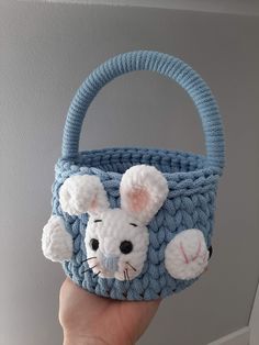 a hand holding a small crocheted basket with a mouse on the front and ears