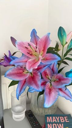 a vase filled with pink and blue flowers sitting on top of a table next to a remote control