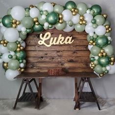 a large balloon arch with the word luka written on it in gold, white and green