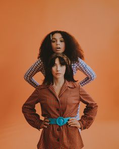 two women standing next to each other in front of an orange background