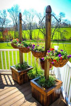 three hanging planters with flowers in them on a wooden deck overlooking a green field