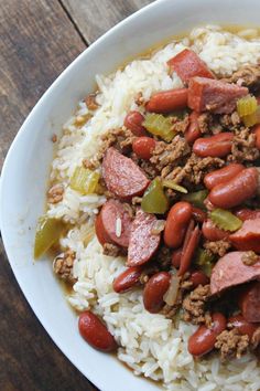 a white bowl filled with rice and sausage on top of a wooden table next to a fork