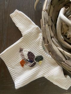 a white knitted sweater next to a basket on a wooden table with branches and twigs