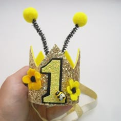 a hand holding a small crown with yellow flowers on it and the number one painted on it