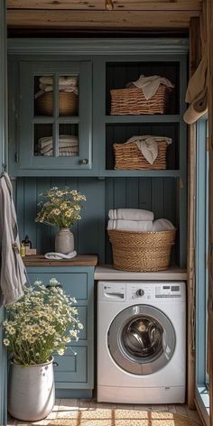 a washer and dryer in a small room with blue cupboards, white towels and flowers