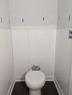 a white toilet sitting inside of a bathroom next to a wall with blue tape on it