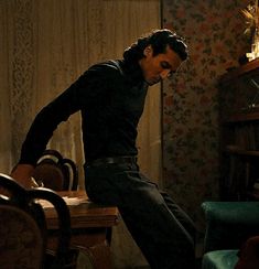 a man standing on top of a wooden table next to a chair and bookshelf