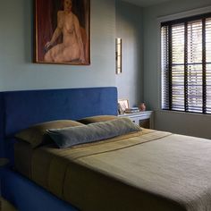 a bedroom with a blue headboard and painting on the wall