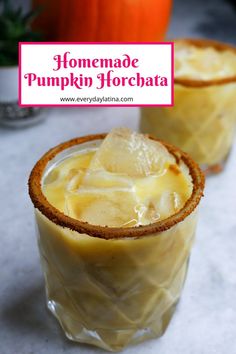 two glasses filled with homemade pumpkin horchata on top of a white table next to an orange pumpkin