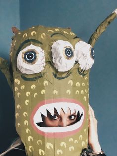 a person holding up a cardboard monster mask