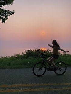 a woman is riding her bike down the road at sunset with the sun in the background