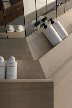 three white containers sitting on top of a counter next to a mirror and soap dispenser