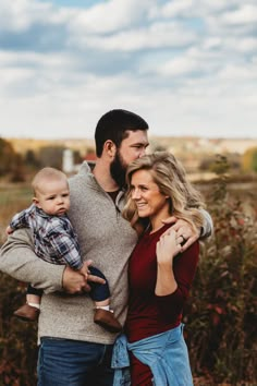 a man and woman holding a baby while standing next to each other in a field