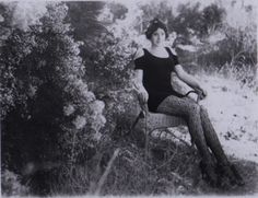 a woman sitting on top of a chair in the grass next to bushes and trees