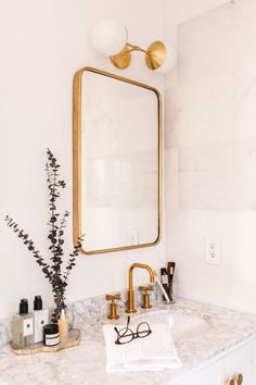 a bathroom with marble counter top and gold framed mirror above the sink, along with accessories