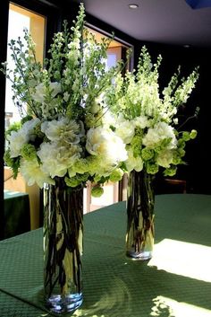 two vases filled with flowers sitting on top of a green tablecloth covered table