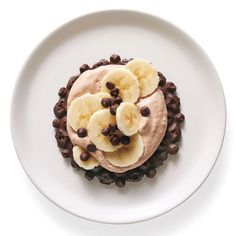 a white plate topped with chocolate chips and banana slices on top of cake covered in frosting